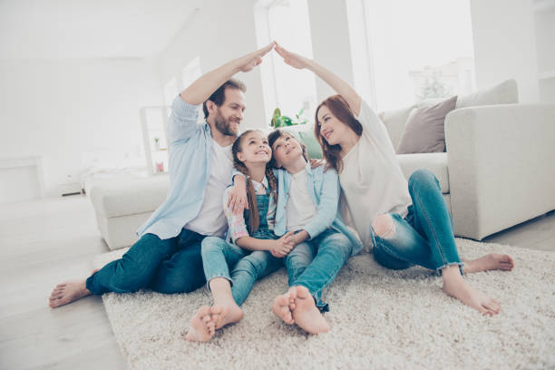 istockphoto-975006448-612x612 New building residential house purchase apartment concept. Stylish full family with two kids sitting on carpet, mom and dad making roof figure with hands arms over heads